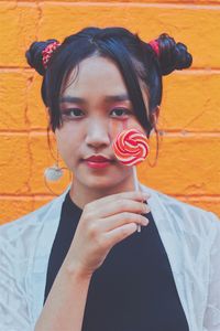 Portrait of young woman having lollipop while standing against orange wall