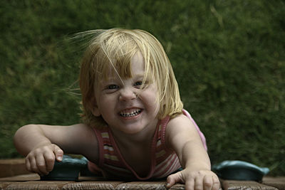 Portrait of girl smiling while climbing wooden fence in yard