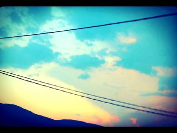 Low angle view of power lines against cloudy sky