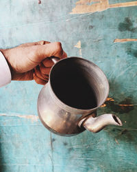 Cropped hand of man holding vintage kettle by weathered blue wall