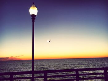 Street light by sea against clear sky during sunset