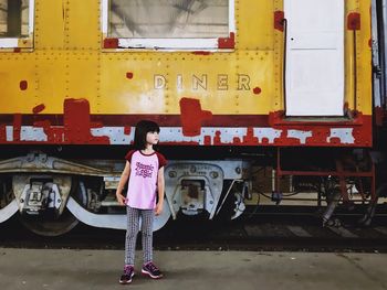 Full length of girl looking away while standing against train