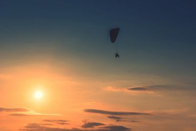 Low angle view of silhouette person paragliding against sky during sunset