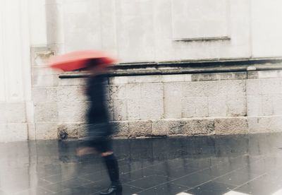 Blurred motion of woman walking on footpath during rainy season
