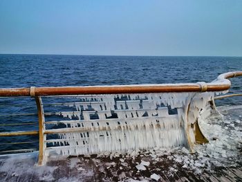 Ice of railing by sea against clear blue sky 