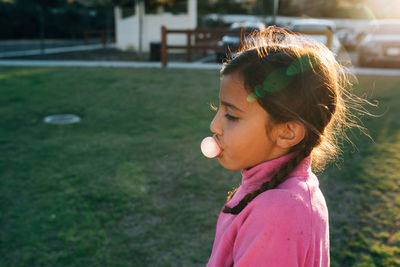 Side view of girl blowing bubble gum at park