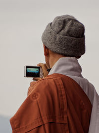 Rear view of man photographing with camera against sky