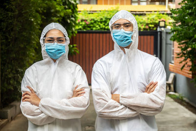 Portrait of man and woman wearing protective suit with mask standing outdoors