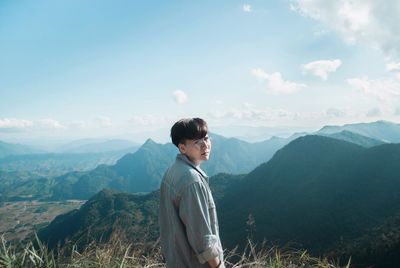 Young man looking at mountains against sky