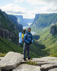 Full length portrait of male hiker standing against mountains on rocks at gros morne national park