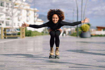 Portrait of smiling woman with arms outstretched roller skating on footpath in city