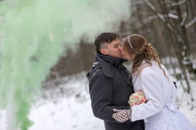 Wedding couple kissing while standing at forest during winter