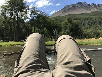 Low section of man relaxing on mountain against sky