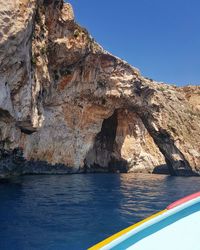 Rock formations by sea against clear blue sky