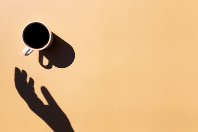 White cup of black espresso coffee top view, shadow, hand holding or touching cup, beige background