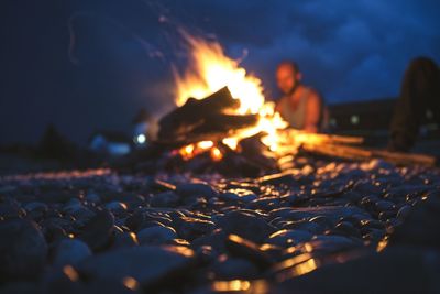 Friends sitting by campfire against sky at dusk