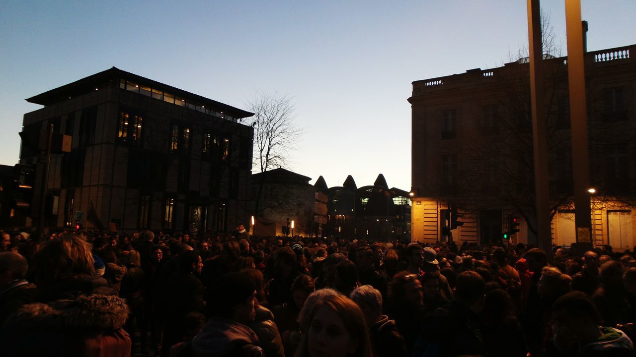 large group of people, building exterior, architecture, crowd, built structure, lifestyles, person, men, clear sky, leisure activity, illuminated, night, silhouette, city, dusk, sky, city life, mixed age range, copy space