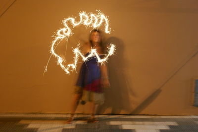 Blurred motion of woman holding illuminated sparkler against wall at night