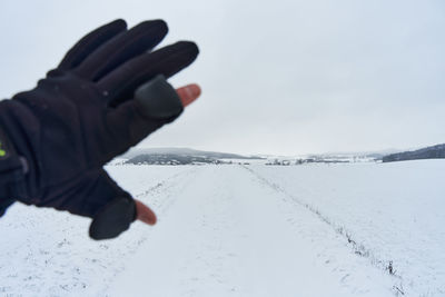 Person hand on snow covered land against sky