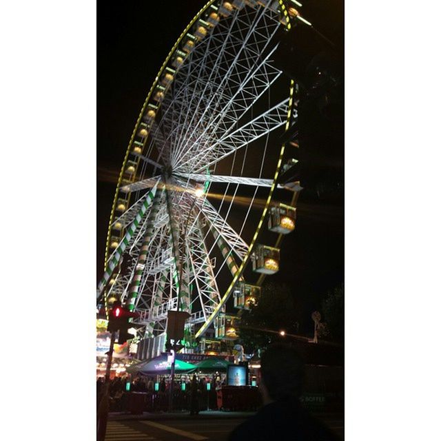 ferris wheel, amusement park, amusement park ride, arts culture and entertainment, transfer print, built structure, architecture, low angle view, night, illuminated, clear sky, building exterior, auto post production filter, city, sky, outdoors, motion, traveling carnival, incidental people, travel destinations