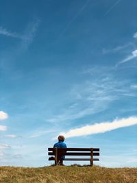 Rear view of man sitting on bench in field