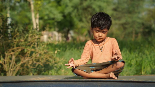 Happy little girl meditates on green field at sunny summer day.