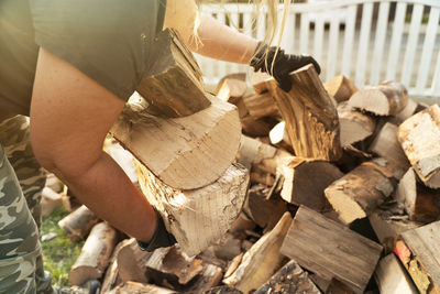 A woman in casual clothes collects beech logs. firewood has been delivered to the front garden. 