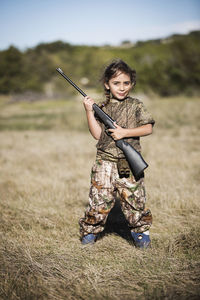 Portrait of confident girl holding rifle on grassy field