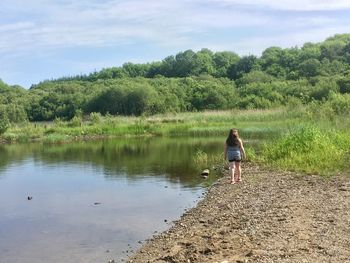 Rear view of girl walking at lakeshore against trees