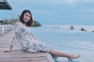 Portrait of smiling woman sitting against sky