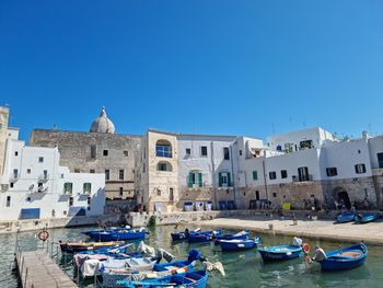 Boats in canal by buildings against clear blue sky
