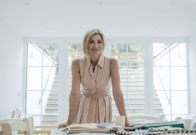 Portrait of female entrepreneur standing near fabric swatches and fashion designs on table