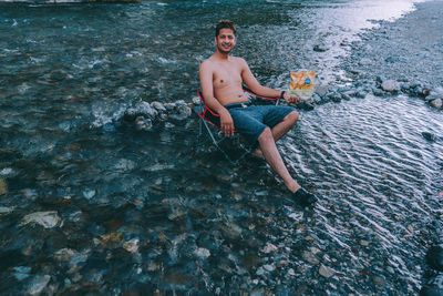 Full length of shirtless young man standing on rock