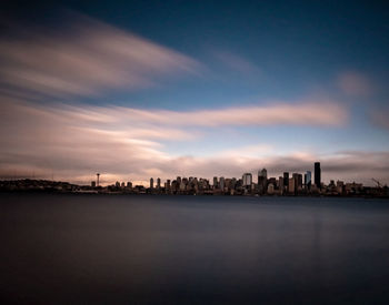 Sea and buildings against sky at dusk