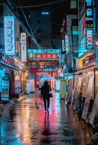 Rear view of woman carrying umbrella in city at night during rain