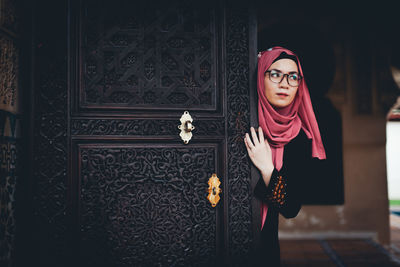 Young woman wearing hijab standing by door