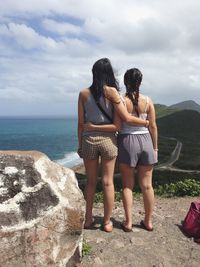 Rear view of friends standing by sea against sky
