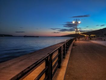 Street by sea against sky at sunset