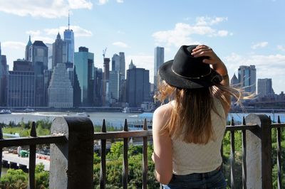 Rear view of woman standing by railing against buildings in city