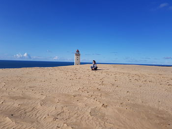 Woman sitting at beach against blue sky