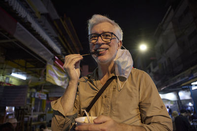 Portrait of smiling senior man eating street food