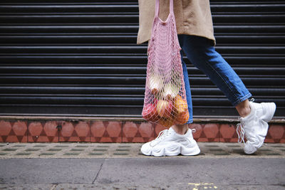 Woman with fruits in mesh bag walking by shutter