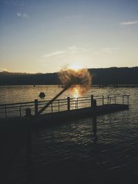 Silhouette railing by lake against sky during sunset