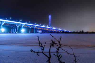 Illuminated bridge over river during winter at night