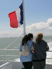 Rear view of women standing on railing against sea