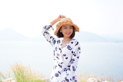 Portrait of smiling young woman standing against sea