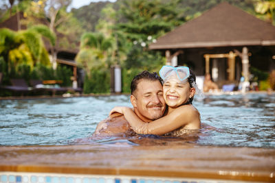 Happy girl embracing father while swimming in pool at resort during vacation
