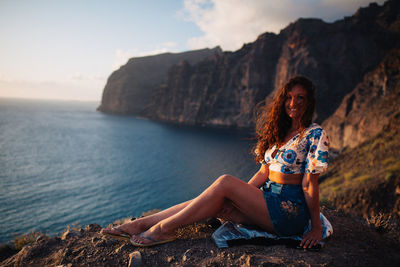 Woman sitting on rock by sea against sky