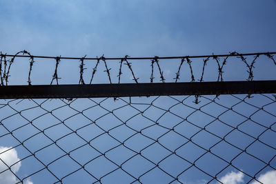 Low angle view of prison fence against blue sky