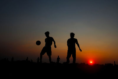 Silhouette people playing with ball against sky during sunset